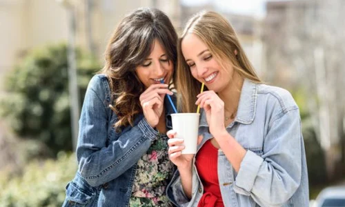 two young women drinking the same take away glass together with two straws outdoors 1139 1624 jpeg