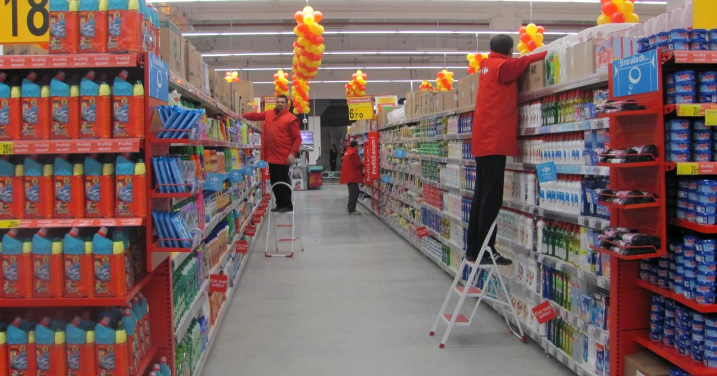 Angajați Carrefour urcați pe scări să pună produsele pe raft