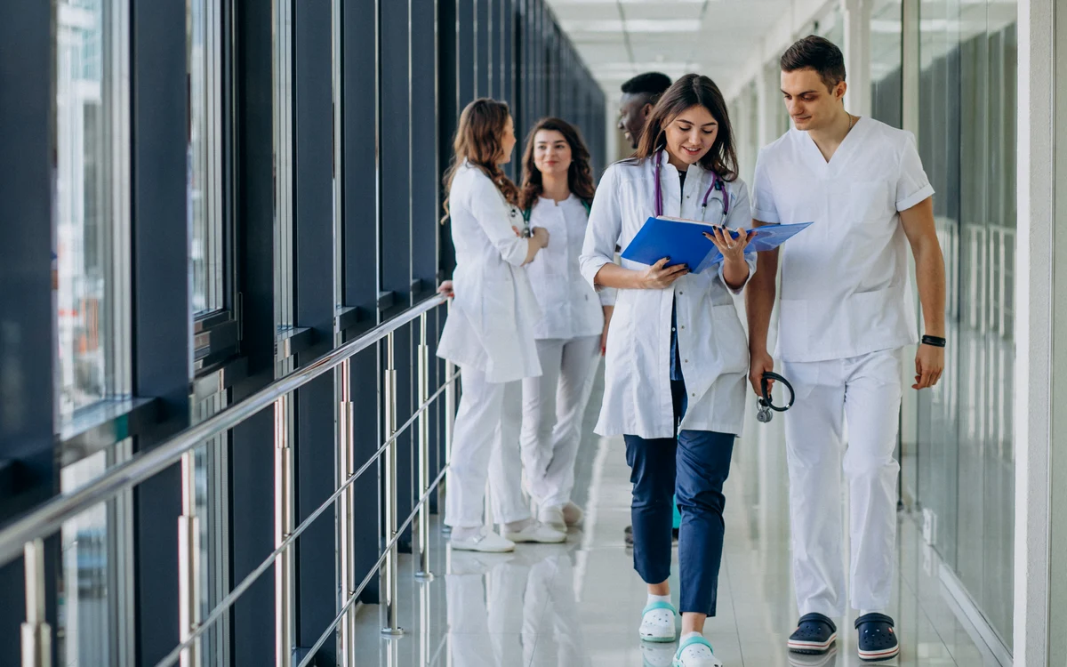 Medici pe holul unui spital, tineri care se uită într-un dosar
