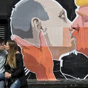 Un cuplu de îndrăgostiţi se sărută în faţa unui perete pe care sunt pictaţi preşedintele Rusiei Vladimir Putin care îl sărută pe candidatul republican la preşedenţia Statelor Unite Donald Trump. FOTO AP