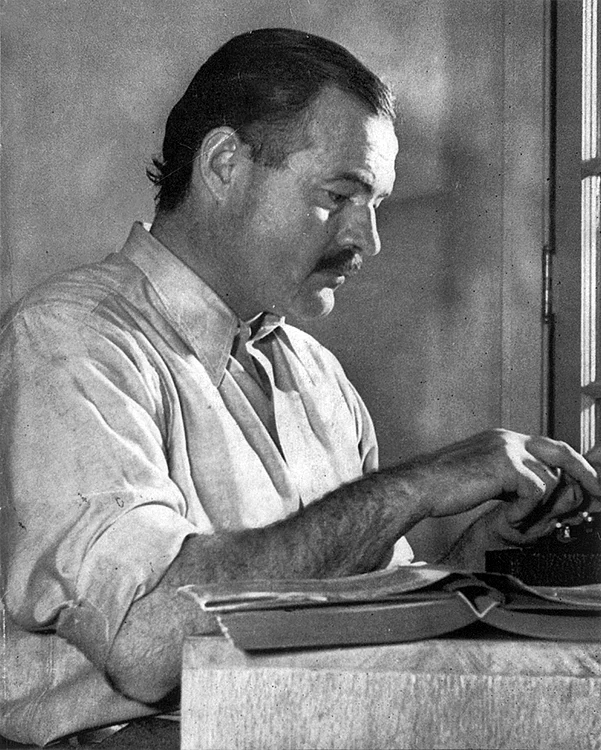 Ernest Hemingway, așezat la masa de lucru (© Lloyd Arnold / Wikimedia Commons)