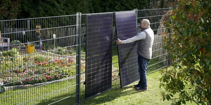 Un bărbat instalează panouri fotovoltaice vertical pe un  gard