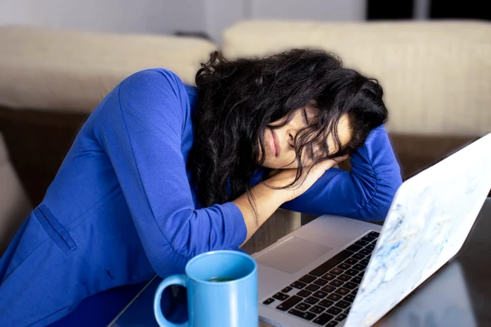 O femeie a adormit în fața laptopului, lângă o cană cu cafea