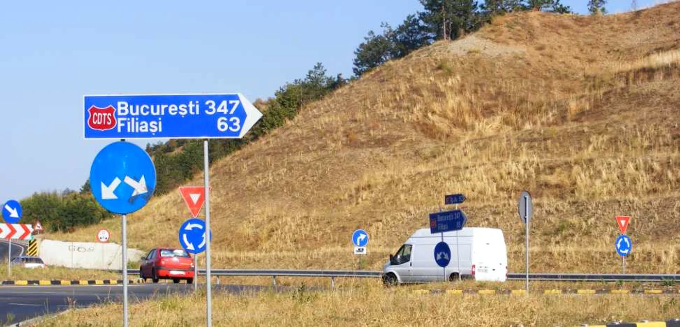 conducătorii auto se uită miraţi la cele două indicatoare rutiere