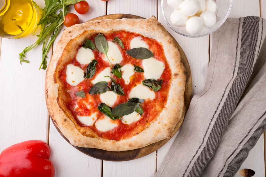 Pizza cu mozzarella și busuioc, pe un blat de lemn, pe o masă