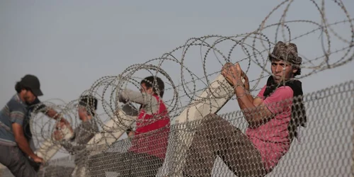 Refugiaţi sirieni urca gardul de sârmă ghimpată de la frontiera dintre Siria şi Turcia în Akçakale provincia Sanliurfa sud-estul Turciei FOTO AP