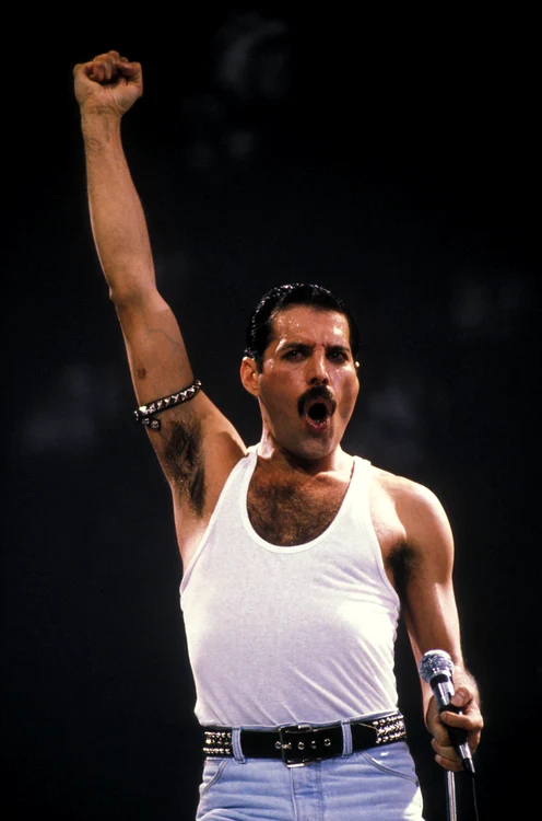 Freddie Mercury, fotografiat în timpul unui concert, îmbrăcat într-un maiou alb și blugi