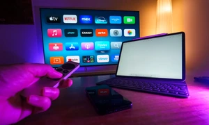 o persoana opereaza telecomanda unui mediaplayer langa un laptop si un televizor in fundal jpg