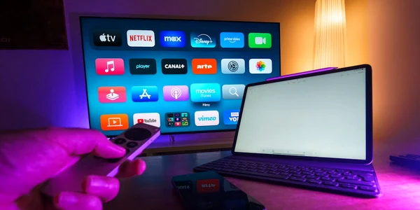 o persoana opereaza telecomanda unui mediaplayer langa un laptop si un televizor in fundal jpg