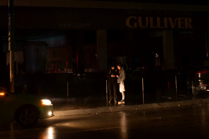 Magazin fără reclamele luminoase aprinse, în fața căruia stau doi tineri