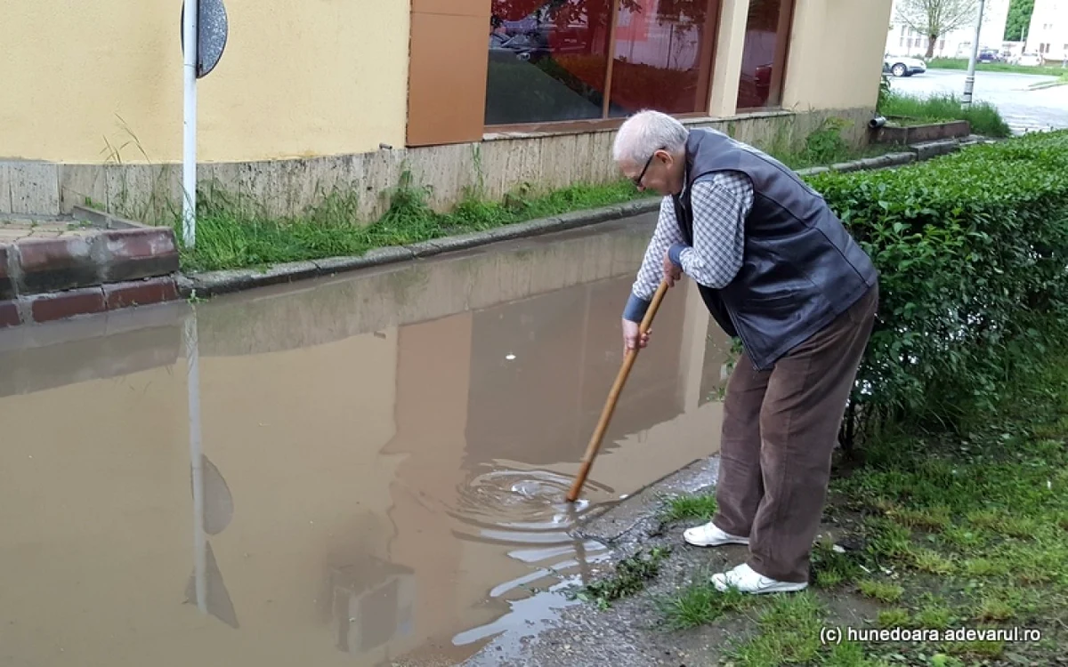 Un hunedorean desfundă canalul care a dus la inundarea străzii. FOTO: Daniel Guţă. ADEVĂRUL.