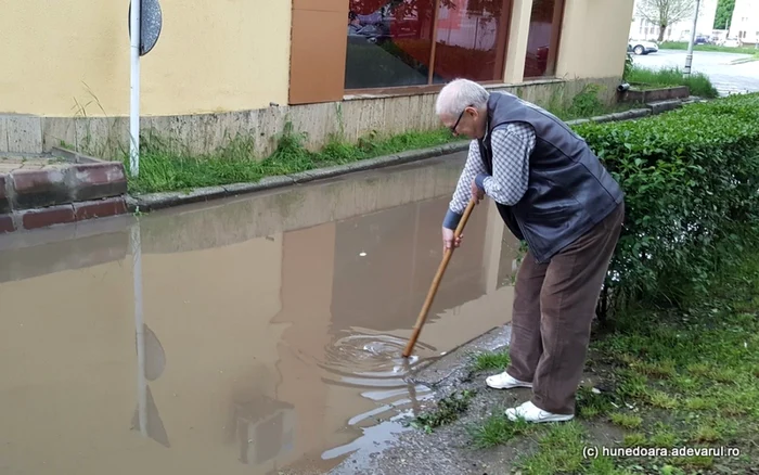 Un hunedorean desfundă canalul care a dus la inundarea străzii. FOTO: Daniel Guţă. ADEVĂRUL.