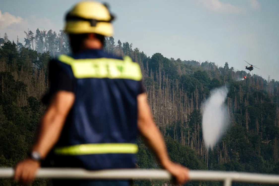 Pompier german priveşte cum un elicopter aruncă apă peste pădurea afectată de incendiu, la graniţa germano-cehă Foto EPA EFE