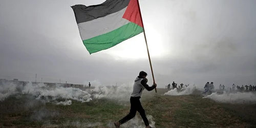Un protestatar purtând un drapel palestinian se fereşte de gazele lacrimogene israeliene în timpul ciocnirilor de lângă graniţa cu Israel în estul oraşului Gaza în Fâşia Gaza Demonstranţii palestinieni au protestat împotriva deciziei preşedintelui am