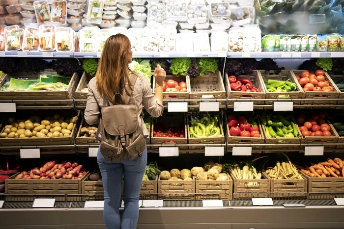O tânără se uită la raionul de fructe și legume dintr-un supermarket