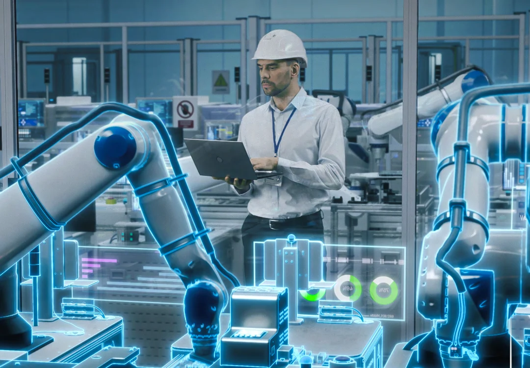 Un inginer supraveghează la un laptop operațiunile roboților dintr-o fabrică