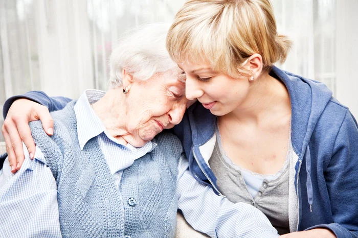 O tânără care alină o persoană în vârstă care probabil suferă de Alzheimer Foto Shutterstock
