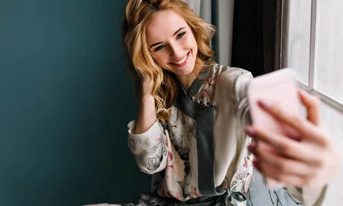morning selfie young beautiful woman happy cheerful girl she wearing silk pajama has wavy blonde hair sitting window sill room with turquoise wall jpg