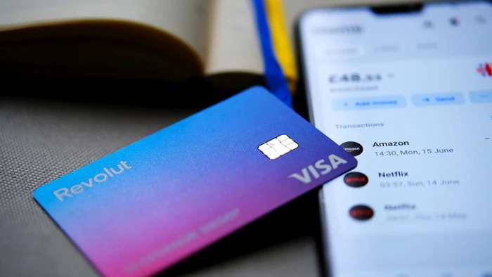 Card Revolut lângă un telefon pe care este deschisă aplicaţia