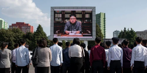 Nord-coreeni se uita la un afis de propaganda cu Kimg Jong-un