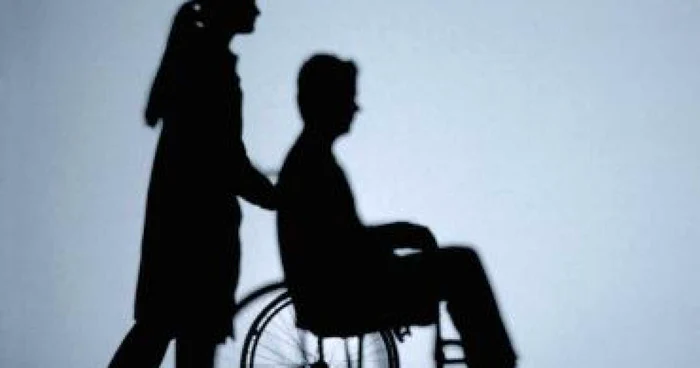Umbra unei tinere care împinge scaunul cu rotile pe care stă un bărbat tânăr