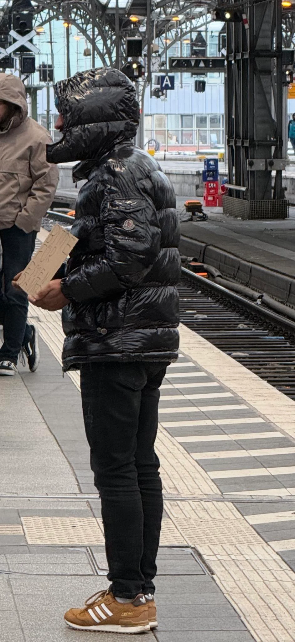 „Așa arată sărăcia în Germania”: cerșetor cu geacă Moncler și pantofi Adidas, filmat în Gara din Köln. Imaginile au stârnit controverse