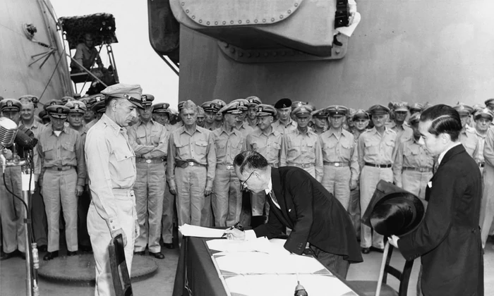 Ministrul de Externe al Japoniei, Mamoru Shigemitsu, semnează capitularea Japoniei, la bordul navei USS Missouri, în fața generalului american Richard K. Sutherland, la 2 septembrie 1945 (© Naval Historical Center Photo # SC 213700)