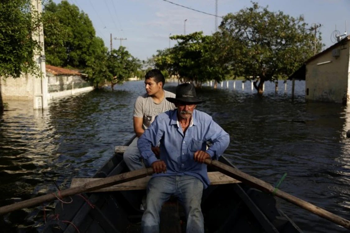 Doi localnici traversând cu o barcă zonele afectate de inundaţii în Paraguay. FOTO AP
