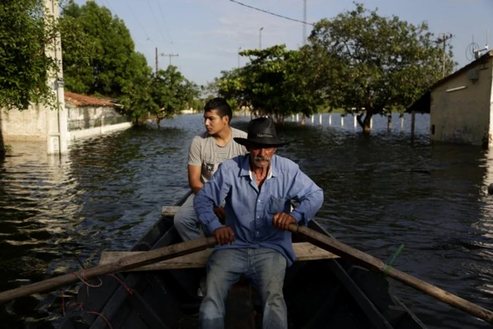 Doi localnici traversând cu o barcă zonele afectate de inundaţii în Paraguay. FOTO AP