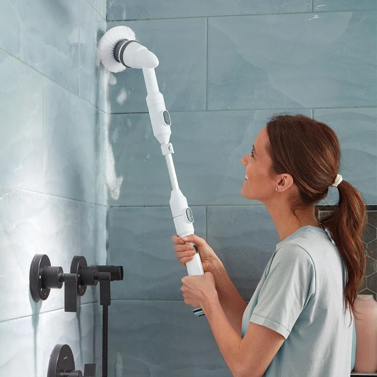 Femeie care folosește o perie electrică de curățare extensibilă pentru rosturile faianței din baie