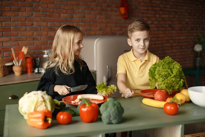 Copii în bucătărrie mâncând legume