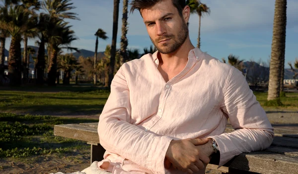 young hispanic male wearing pink shirt posing beach near palm trees jpg