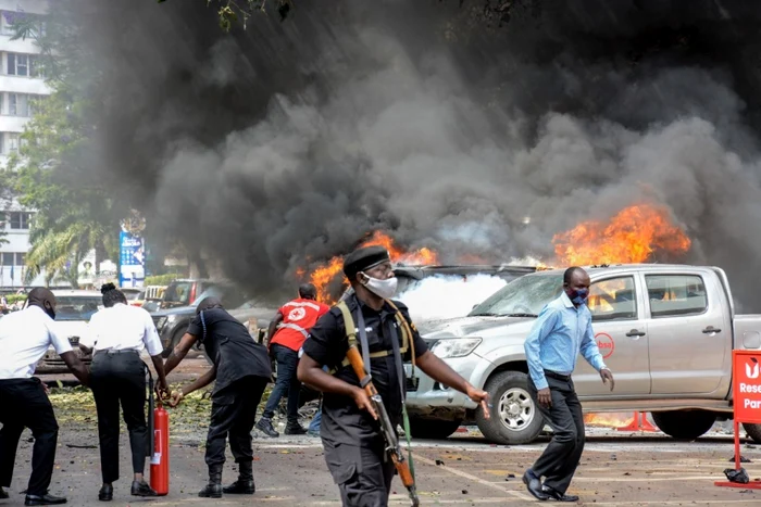 FOTO: AFP / Oamenii sting focul de pe maşini provocat de explozia unei bombe în apropierea clădirii Parlamentului din Kampala, Uganda, 16 noiembrie 2021.