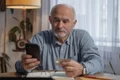 un barbat in varsta se uita pe un telefon mobil tinand in amna un card de credit jpg