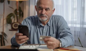 un barbat in varsta se uita pe un telefon mobil tinand in amna un card de credit jpg