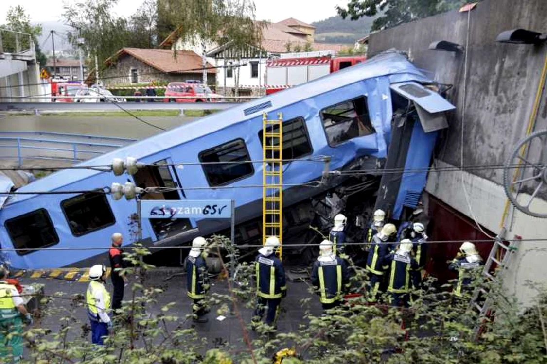 
    Pompierii spanioli se luptă să scoată cadavrul conductorului dintre fiarele contorsionate ale trenului  