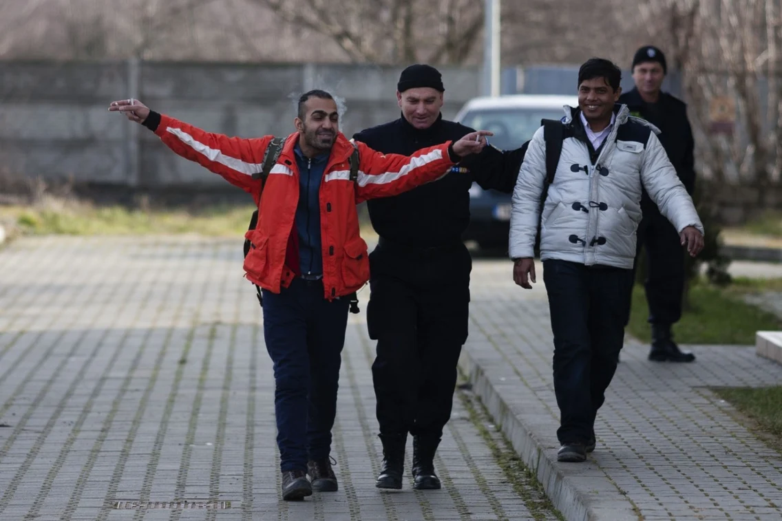 Un imigrant ilegal reacţionează la vederea camerelor TV în timp ce este escortat de un jandarm prin curtea sediului Poliţiei de Frontieră din localitatea Jimbolia