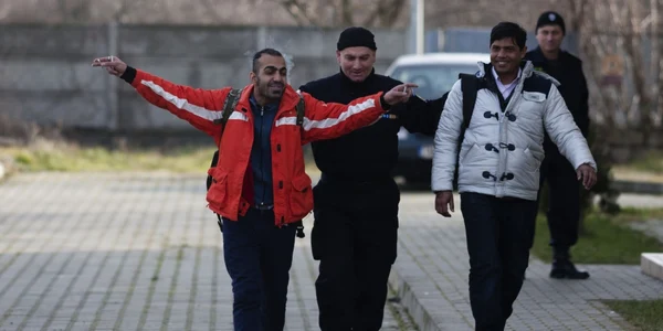 Un imigrant ilegal reacţionează la vederea camerelor TV în timp ce este escortat de un jandarm prin curtea sediului Poliţiei de Frontieră din localitatea Jimbolia