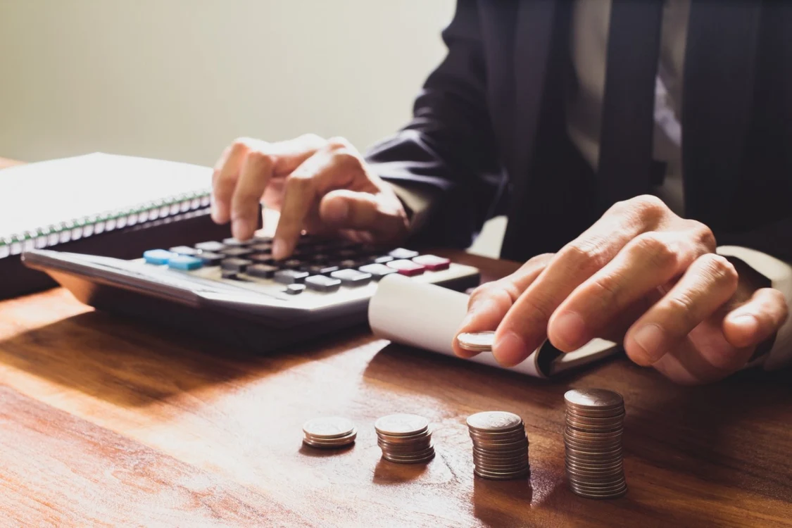 un barbat face niste calcule in timp ce numără monede lângă calculator