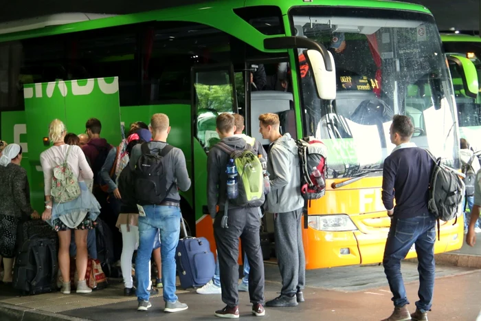 Turiști care așteaptă să se urce într-un autocar după ce au încărcat bagajele