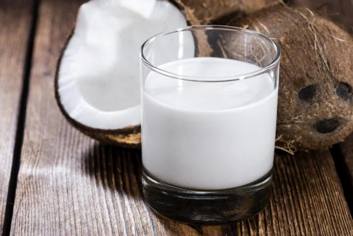 Laptele de cocos într-un pahar lângă o nucă și jumătate de cocos Foto mancarecucap