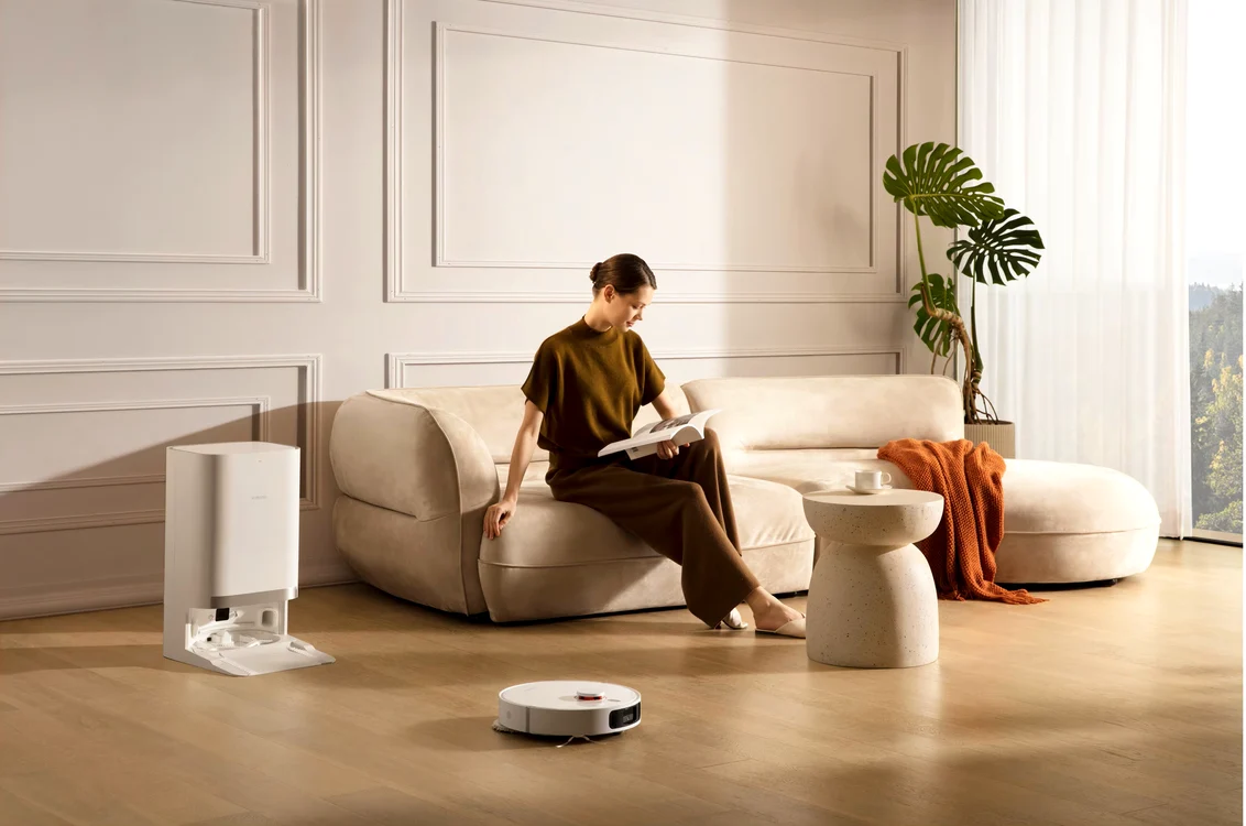 Tânără citește pe canapea în timp ce aspiratorul robot curăță casa