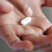 white pill being taken from palm of hand webp