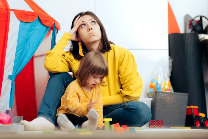 Mama îngrijorată și streasată alături de un copil care se joacă