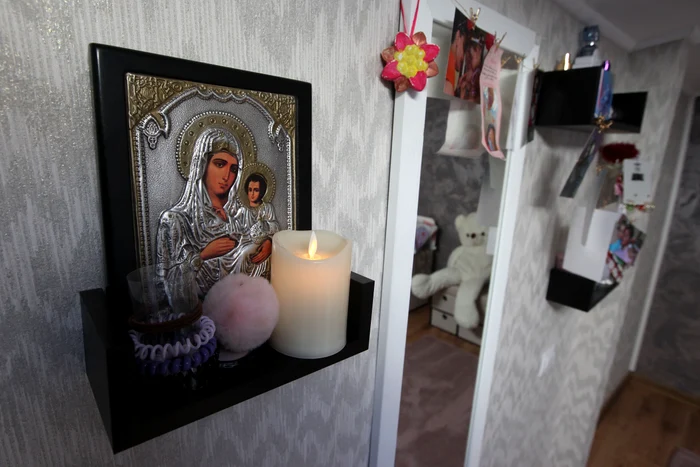 Pe peretele camerei, lumânarea arde neîncetat sub o iconiță cu Maica Domnului