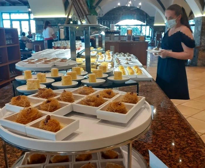 Turiștii se servesc singuri cu bunătăți, după ce-și pun mănuși de unică folosință. Masca se poartă până la masă