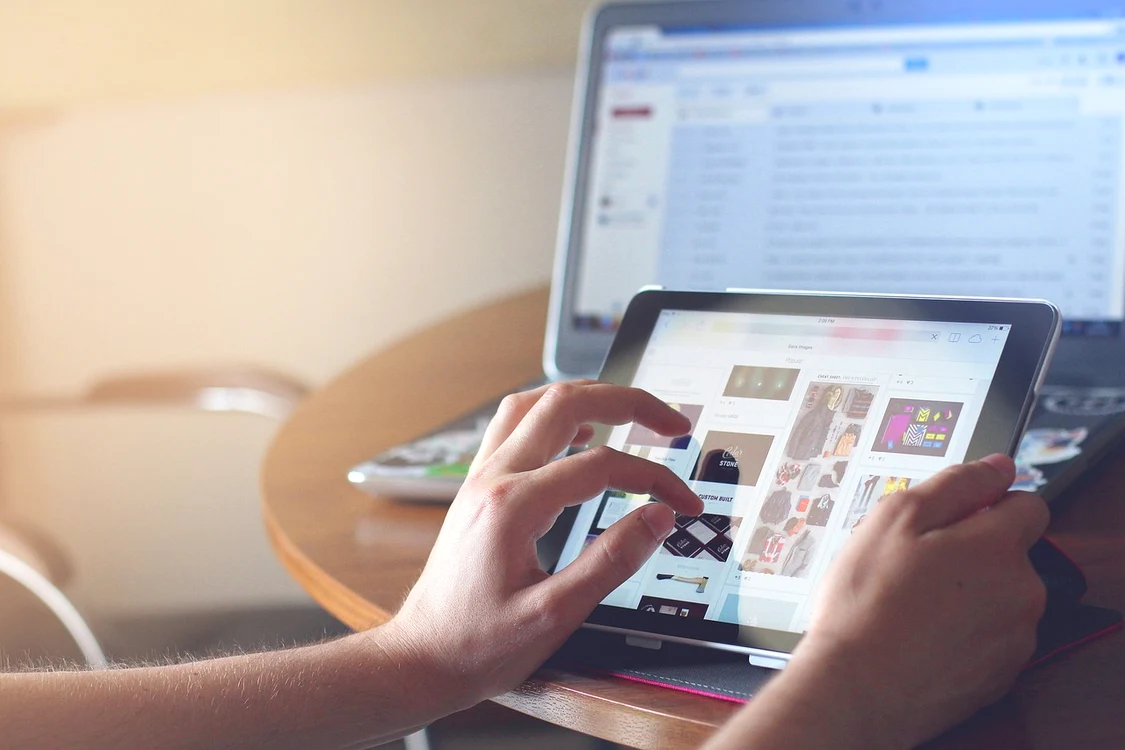Cineva tastează ceva pe o tabletă în fața unui laptop