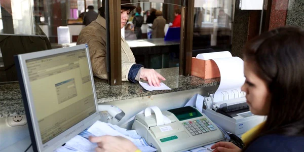 Oameni de diferite vârste stau în rând la poșta centrală ca să achite facturile