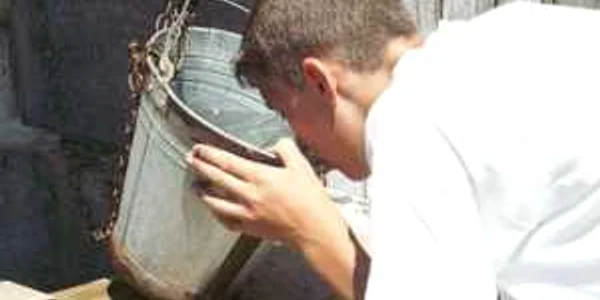 Un tânăr de la ţară bea însetat apă dintr-o fântână 
