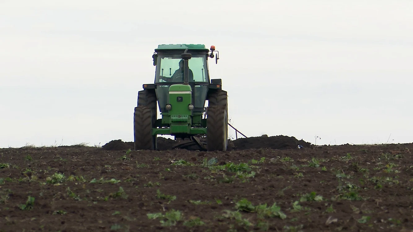 Un tractor verde care ară pe un câmp